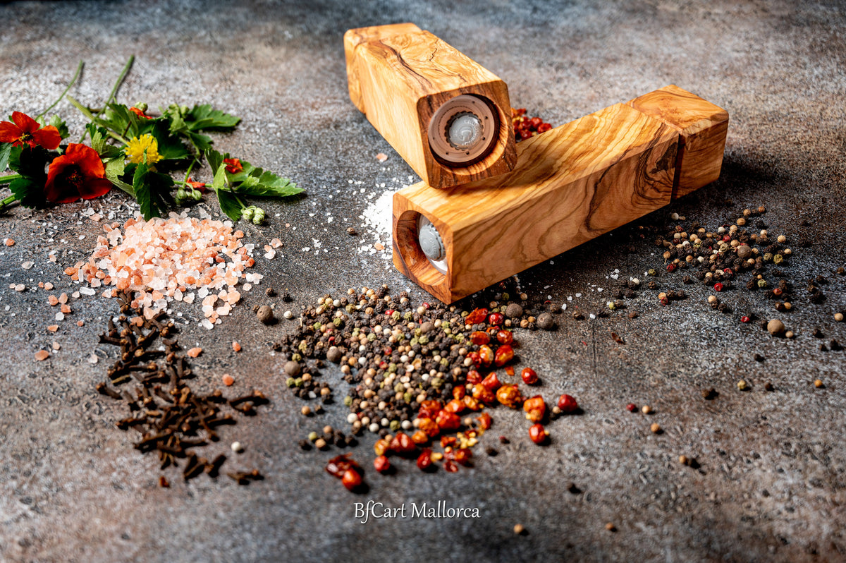 Olive wood pepper shaker on a table with design and square shape. Side view, with peppers and salt on the table, different pepper shakers on the table.
