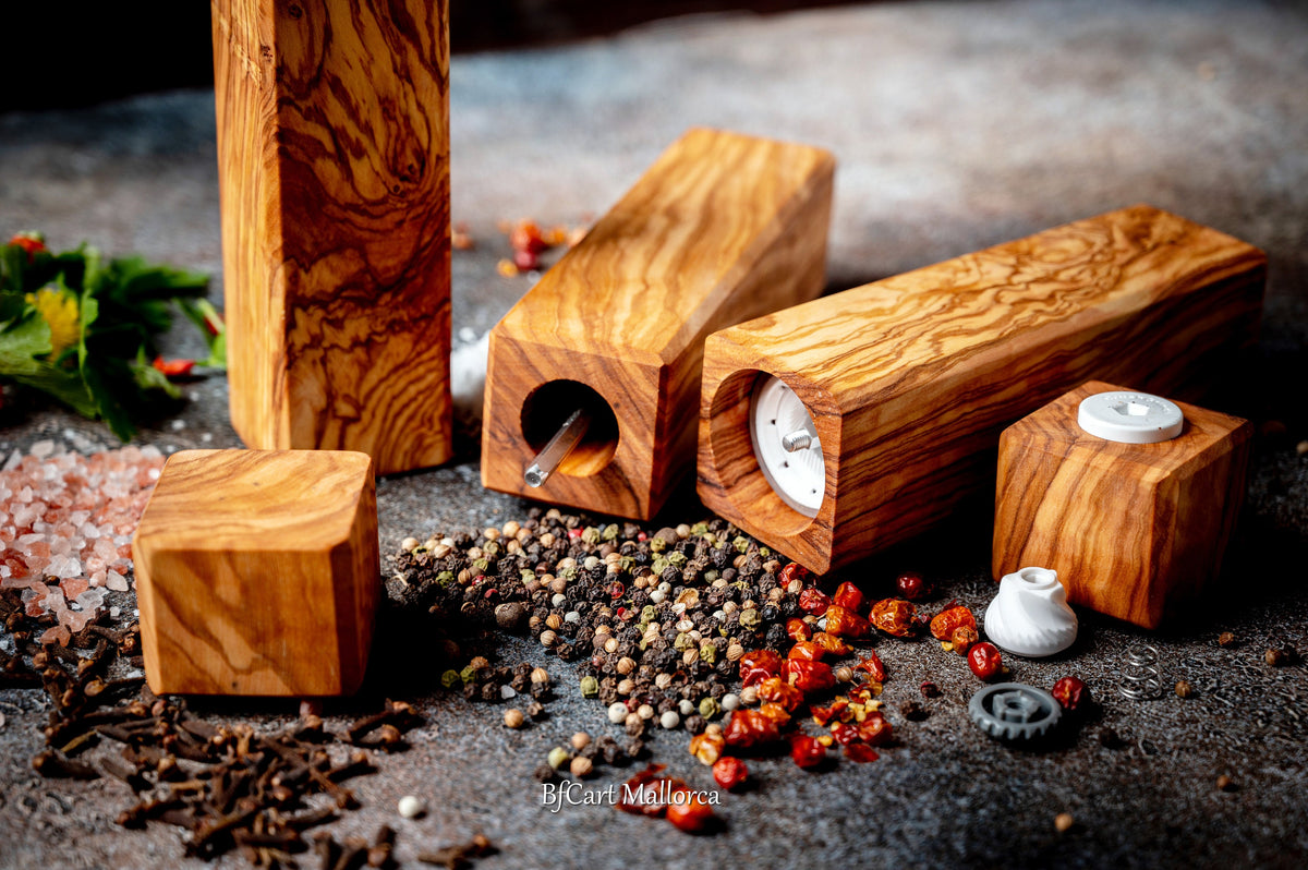 Olive wood pepper shaker on table with design and square shape. Side view, with peppers and salt on the table, different pepper shakers on the table. Disassembled pepper shaker shows the ceramic grinding mechanism.