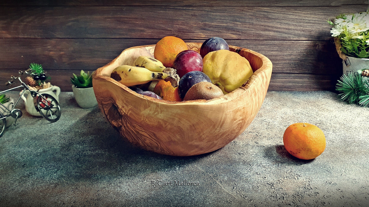 Large salad bowl or round fruit bowl made of rustic olive wood, with irregular shapes of the trunk, Salad bowl with highly grained wood drawings. Medium brown colour. Irregular salad bowl filled with fruit. Fruit bowl full of fruits, in a kitchen.