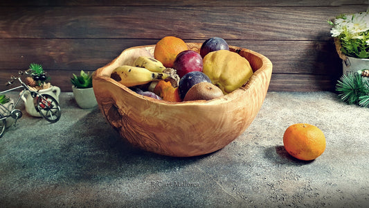 Large salad bowl or round fruit bowl made of rustic olive wood, with irregular shapes of the trunk, Salad bowl with highly grained wood drawings. Medium brown colour. Irregular salad bowl filled with fruit. Fruit bowl full of fruits, in a kitchen.