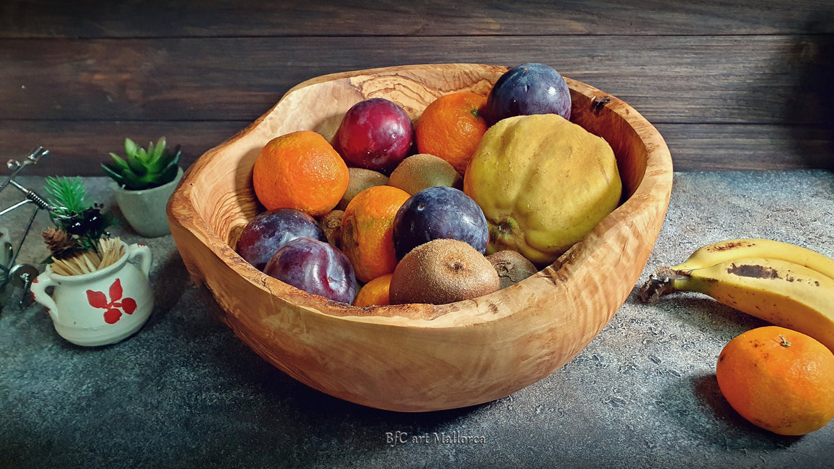 Large salad bowl or round fruit bowl made of rustic olive wood, with irregular shapes of the trunk, Salad bowl with highly grained wood drawings. Medium brown colour. Irregular salad bowl filled with fruit. Fruit bowl full of fruits, in a kitchen
