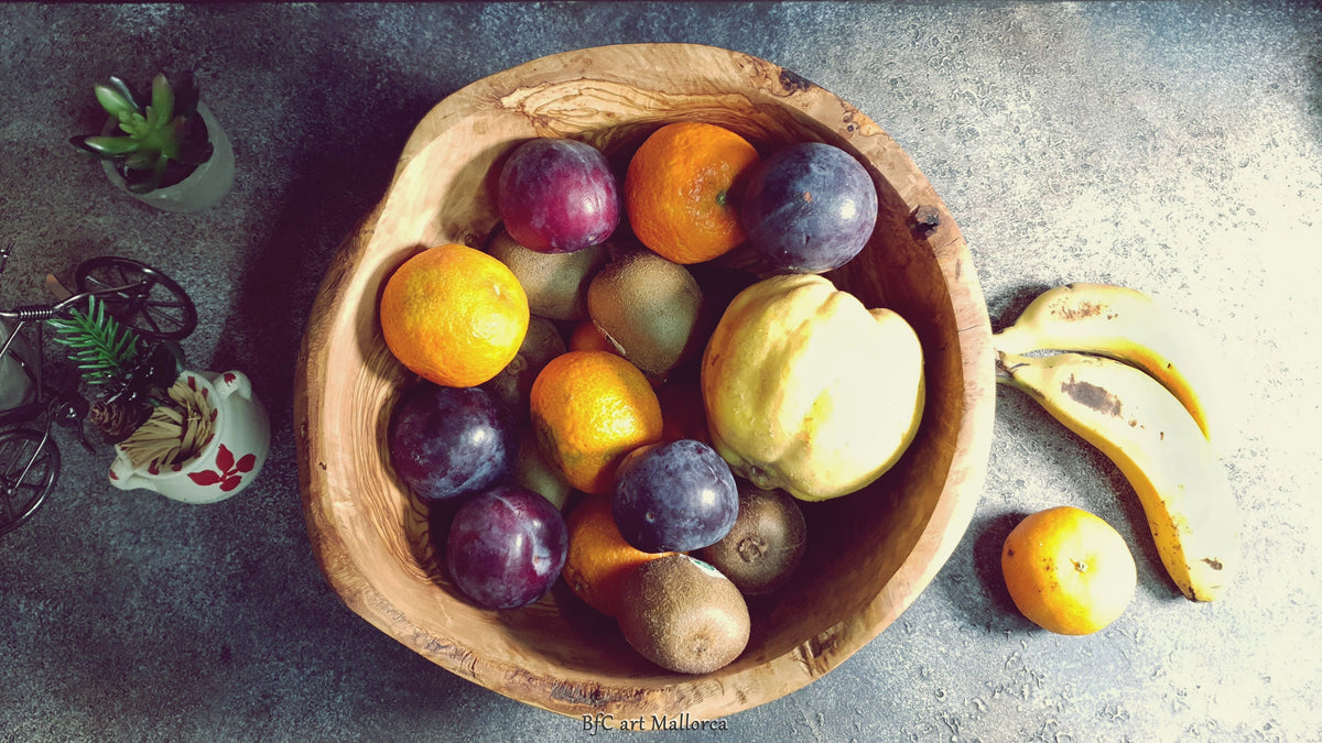 Large salad bowl or round fruit bowl made of rustic olive wood, with irregular shapes of the trunk, Salad bowl with highly grained wood drawings. Medium brown colour. Irregular salad bowl filled with fruit. Fruit bowl full of fruits, in a kitchen top