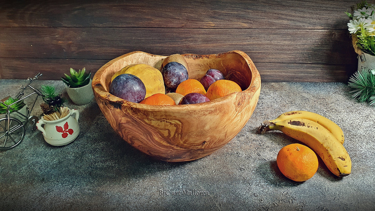 Large salad bowl or round fruit bowl made of rustic olive wood, with irregular shapes of the trunk, Salad bowl with highly grained wood drawings. Medium brown colour. Irregular salad bowl filled with fruit. Fruit bowl full of fruits, in a kitchen